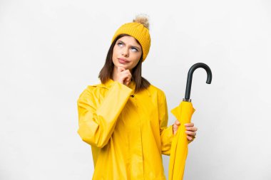 Young Russian woman with rainproof coat and umbrella over isolated white background and looking up