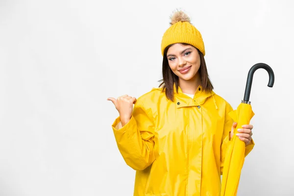 製品を提示するために側面を指して隔離された白い背景の上にレインプルーフコートと傘を持つ若いロシアの女性 — ストック写真