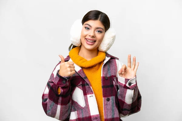 stock image Young Russian woman wearing winter muffs over isolated white background showing ok sign and thumb up gesture