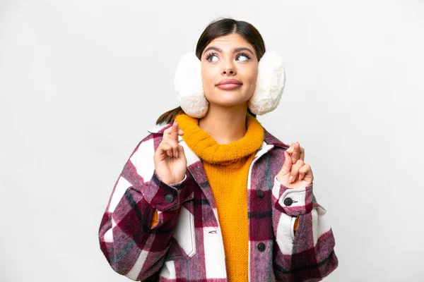 Young Russian woman wearing winter muffs over isolated white background with fingers crossing