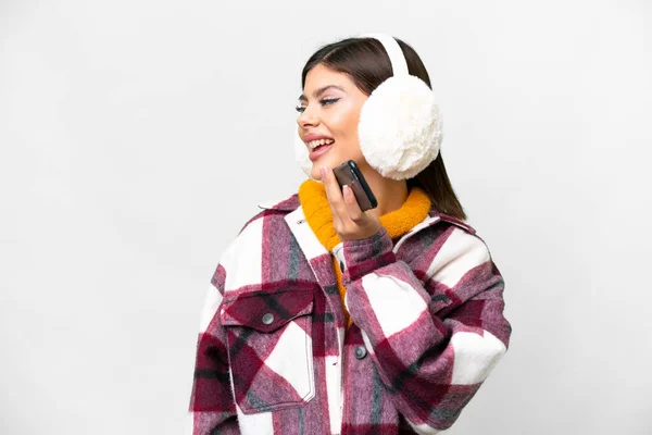 stock image Young Russian woman wearing winter muffs over isolated white background keeping a conversation with the mobile phone with someone