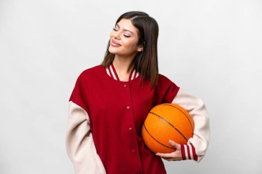 İzole edilmiş beyaz arka planda basketbol oynayan genç Rus kadın yana bakıyor ve gülümsüyor.