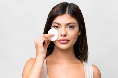 Young Russian woman over isolated white background with cotton pad for removing makeup from her face