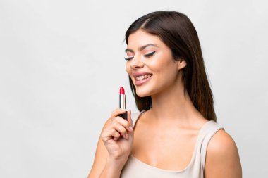 Young Russian woman over isolated white background holding red lipstick