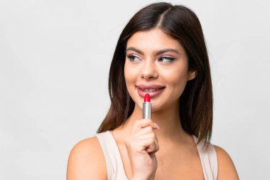 Young Russian woman over isolated white background holding red lipstick