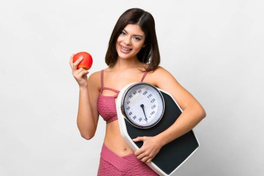 Young Russian woman over isolated white background with weighing machine and with an apple