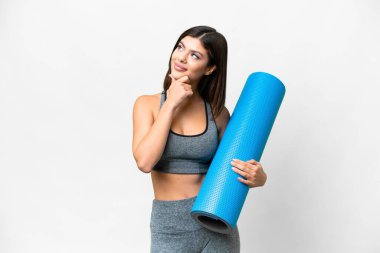 Young sport woman going to yoga classes while holding a mat over isolated white background having doubts
