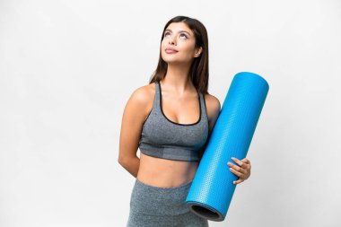 Young sport woman going to yoga classes while holding a mat over isolated white background and looking up