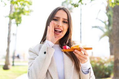Genç ve güzel bir kadın açık havada sashimi tutuyor ve ağzı açık bağırıyor.