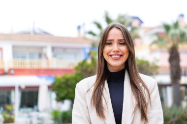 Genç, güzel bir kadın açık havada, mutlu bir ifadeyle.