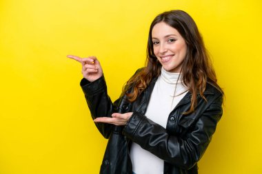 Sarı arka planda izole edilmiş genç beyaz kadın bir ilan vermek için avucunun içinde hayali bir mekan tutuyor.