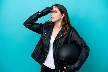 Mavi arka planda izole edilmiş motosiklet kasklı beyaz bir kadın yan tarafa bakarken sürpriz jest yapıyor.