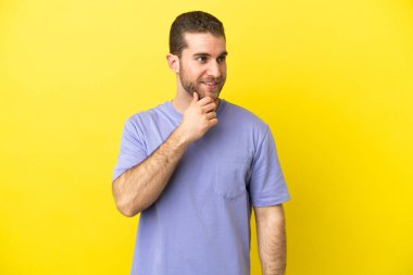 Sarışın yakışıklı adam izole edilmiş sarı arka planda yan tarafa bakıyor ve gülümsüyor.