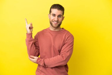 Sarışın yakışıklı adam izole edilmiş sarı arka planda mutlu ve dik duruyor.