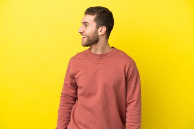 Sarışın yakışıklı adam sarı arka planda. Yan pozisyonda gülüyor.