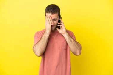 Sarışın yakışıklı adam, izole edilmiş arka planda, yorgun ve hasta bir ifadeyle cep telefonu kullanıyor.