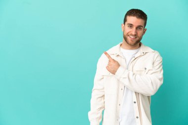 Handsome blonde man over isolated blue background pointing to the side to present a product