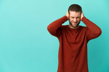 İzole edilmiş mavi arka planda yakışıklı sarışın adam hayal kırıklığına uğramış ve kulaklarını kapatmış.