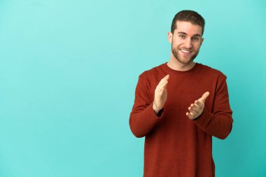 Sarışın, soyutlanmış, mavi arka planda yakışıklı bir adam bir konferanstan sonra alkışlıyor.