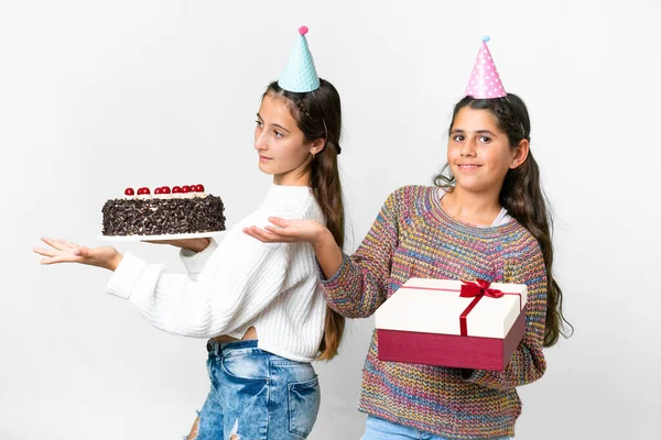 Friends girls holding gift and a birthday cake over isolated white background pointing back and presenting a product