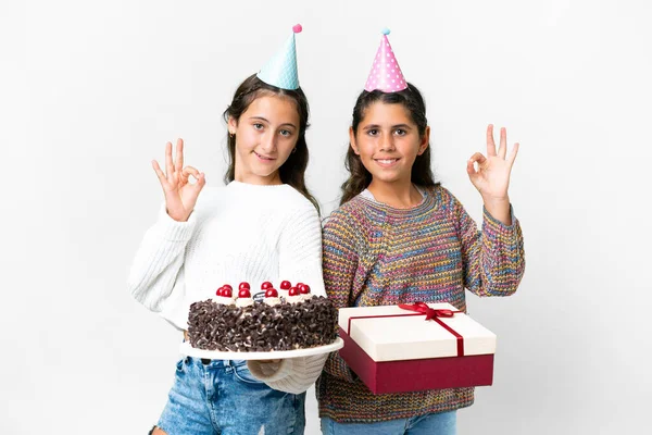 朋友们带着礼物和生日蛋糕的女孩们站在孤独的白色背景上 手指头上挂着一个好的标志 — 图库照片