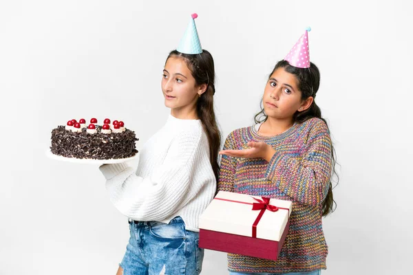 Friends girls holding gift and a birthday cake over isolated white background extending hands to the side for inviting to come