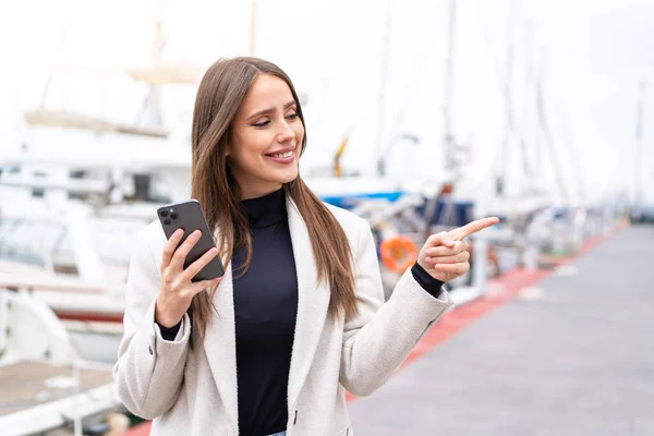 stock image Young pretty woman using mobile phone at outdoors pointing to the side to present a product