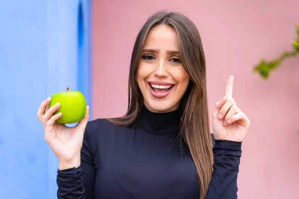 stock image Young pretty woman with an apple at outdoors pointing up a great idea