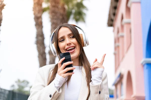 아름다운 아가씨 밖에서 핸드폰으로 음악을 노래를 부르는 — 스톡 사진