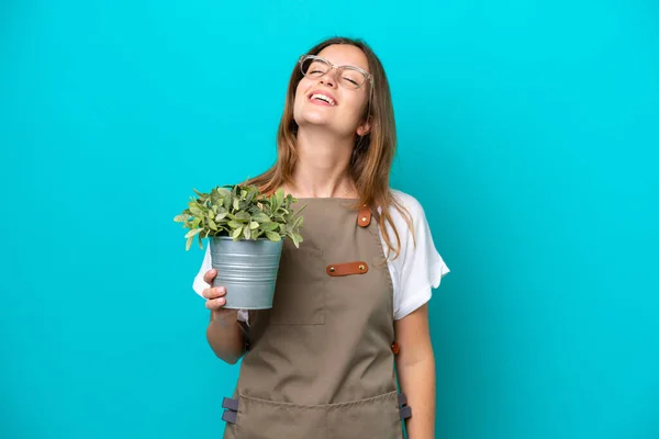 Młody Biały Ogrodnik Kobieta Trzyma Roślina Odizolowany Niebieski Tło Śmiech — Zdjęcie stockowe