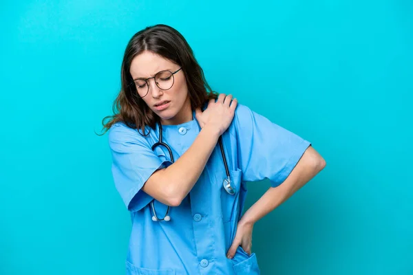 一位年轻的外科医生妇女 因努力工作而因肩部疼痛而被隔离在蓝色背景下 — 图库照片