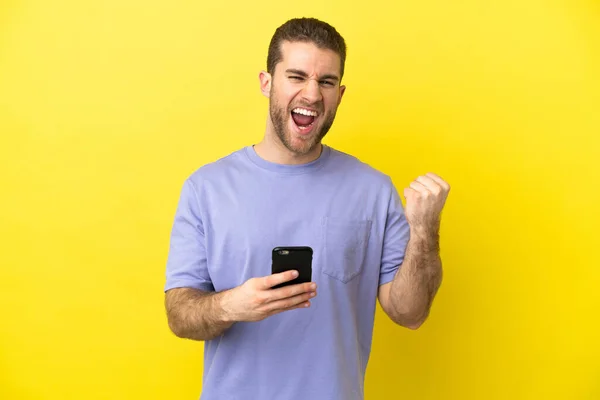 Handsome Blonde Man Isolated Yellow Background Phone Victory Position — Stock Photo, Image