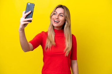 Sarı arka planda izole edilmiş genç Uruguaylı kadın selfie çekiyor.