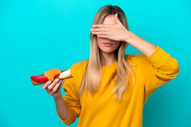 Elinde sashimi tutan genç Uruguaylı kadın mavi arka planda gözlerini elleriyle kapatıyor. Bir şey görmek istemiyorum.