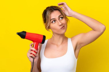 Genç Uruguaylı kadın elinde saç kurutma makinesiyle Don sarı arka planı izole ediyor. Şüpheleri var ve kafası karışık.