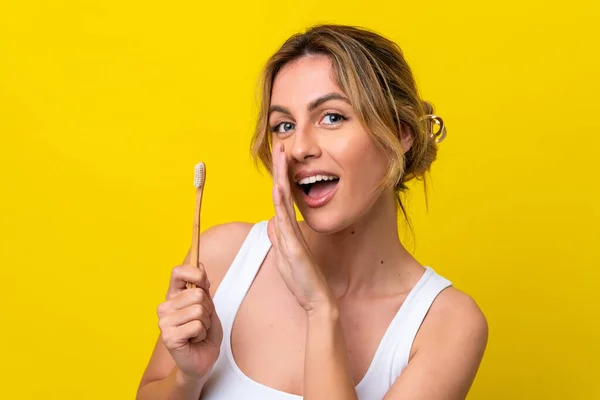 Młoda Urugwajska Kobieta Myjąca Zęby Żółtym Tle Szepcząc Coś — Zdjęcie stockowe