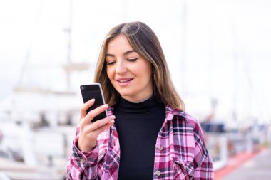 Genç, güzel Romen kadın açık havada cep telefonuyla mesaj ya da e-posta gönderiyor