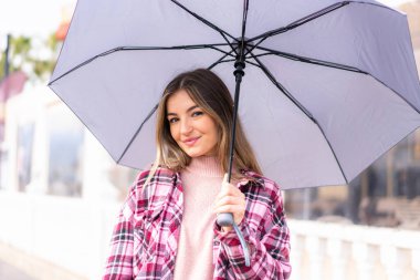 Genç ve güzel Romen kadın elinde şemsiyeyle dışarıda neşeli bir ifade ile bekliyor