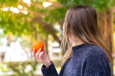 Genç, güzel Romen kadın arka tarafta elinde portakal tutuyor.