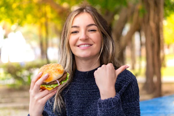 Młoda Ładna Rumuńska Kobieta Trzyma Hamburgera Świeżym Powietrzu Wskazując Bok — Zdjęcie stockowe