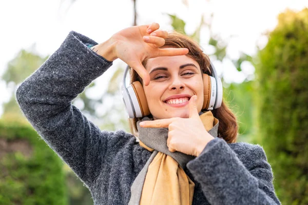 屋外の焦点面でヘッドフォンで音楽を聴いているブルネットの女性 フレーミングシンボル — ストック写真
