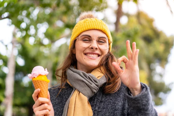 stock image Brunette woman with a cornet ice cream at outdoors showing ok sign with fingers