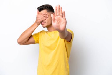 Beyaz arka planda izole edilmiş genç beyaz adam jesti durduruyor ve yüzünü kapatıyor.
