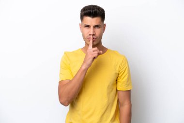 Beyaz arka planda izole edilmiş genç beyaz bir adam sessizlik işareti gösteriyor. Parmağını ağzına sokuyor.