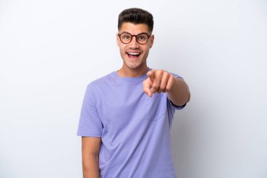 Beyaz arka planda izole edilmiş genç beyaz adam şaşırmış ve ön tarafı işaret ediyor.