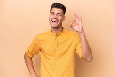 Beyazlı genç adam bej arka planda izole edilmiş. Parmaklarıyla tamam işareti gösteriyor.