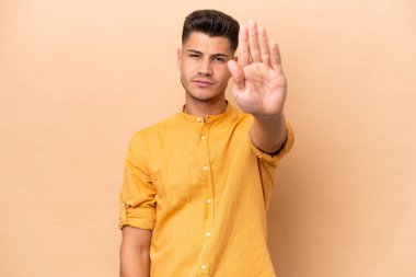 Beyazlı genç bir adam bej arka planda izole edilmiş. Durma hareketi yapıyor.