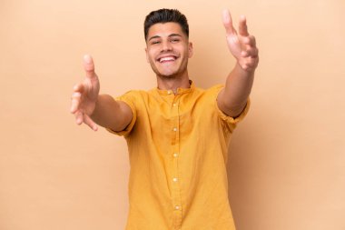 Young caucasian man isolated on beige background presenting and inviting to come with hand
