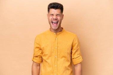 Beyazlı genç bir adam bej arka planda izole edilmiş ve ağzı açık bir şekilde öne doğru bağırıyor.