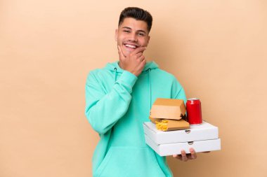 Fast food tutan beyaz bir adam bej arka planda izole edilmiş mutlu ve gülümsüyor.